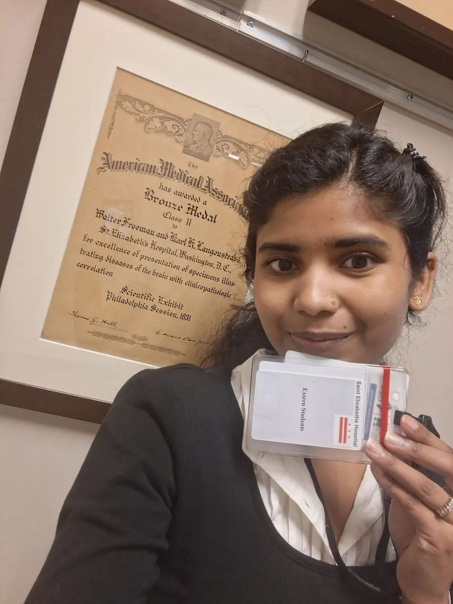 Dr. Aditi Pajiyar holding her extern badge beside a historic American Medical Association award on display at St. Elizabeths Hospital